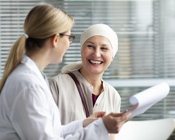 Eine Ärztin spricht mit einer Patientin, die ein Kopftuch trägt. Beide lächeln und scheinen ein Gespräch zu führen.