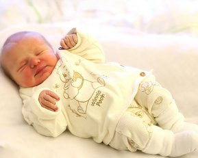 Neugeborenes Baby in einem weißen Winnie-Pooh-Outfit, das auf einer weichen Unterlage liegt und schläft.