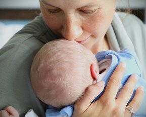 Eine Mutter küsst ihr neugeborenes Baby, das in ihren Armen liegt, während sie liebevoll auf es schaut.