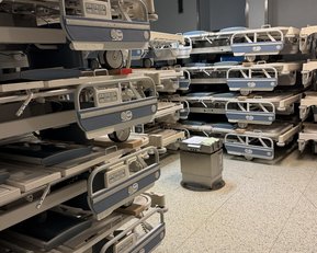 Ein Raum mit mehreren Krankenhausbetten, ordentlich gestapelt und bereit zur Nutzung. Ein kleiner Tisch steht in der Mitte.