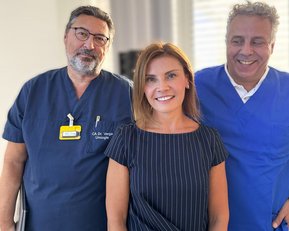Drei medizinische Fachkräfte stehen zusammen, zwei Männer in blauen und schwarzen Kitteln und eine Frau in gestreiftem Oberteil, lächelnd.